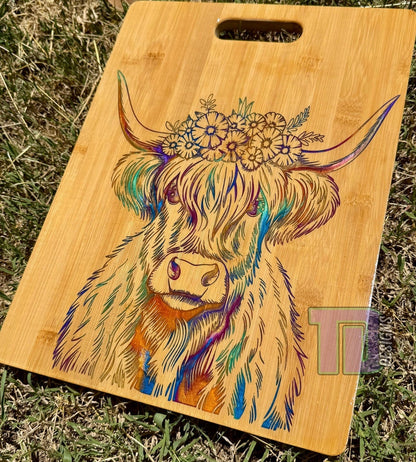 Wooden cutting board with a colorful cow design on grass