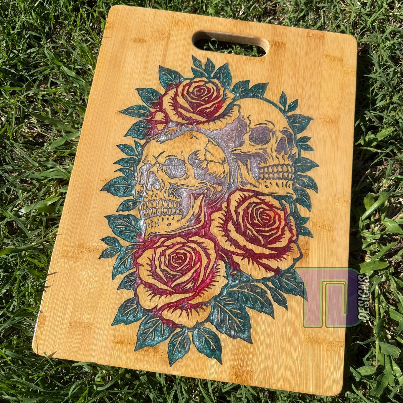 Wooden cutting board with skull and rose design on grass